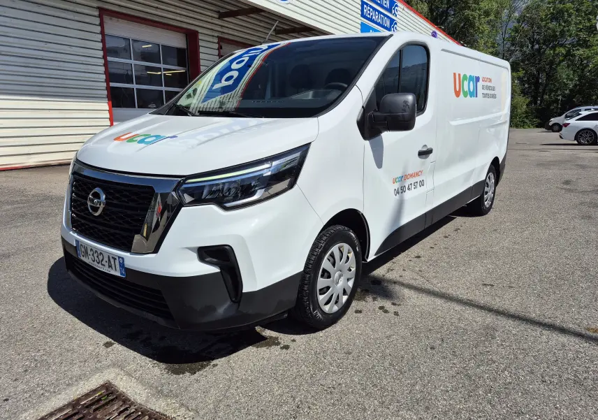 Nissan Primastar blanc en 3/4 avant droit, utilitaire avec logo coloré Ucar sur la porte latérale.