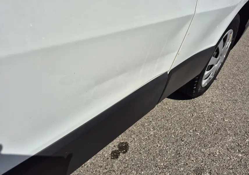 Détail du côté droit arrière blanc du Nissan Primastar avec une rayure visible sur la porte et une roue partielle.