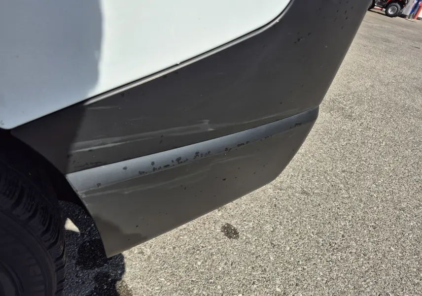 Gros plan sur l'angle arrière droit du Nissan Primastar blanc, montrant un pare-chocs noir avec des traces d'usure.