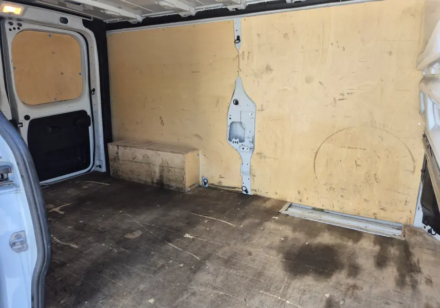 Vue intérieure arrière du fourgon blanc Nissan Primastar, montrant l'espace de chargement avec parois en bois et sol marqué.