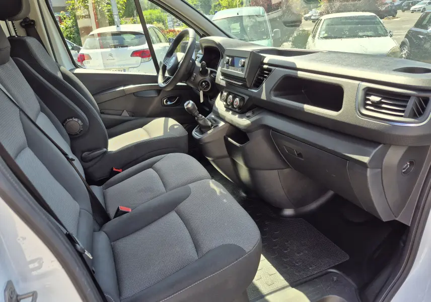 Vue intérieure côté conducteur du Nissan Primastar blanc, montrant les sièges avant, le volant multifonction et la console centrale avec boîte manuelle.