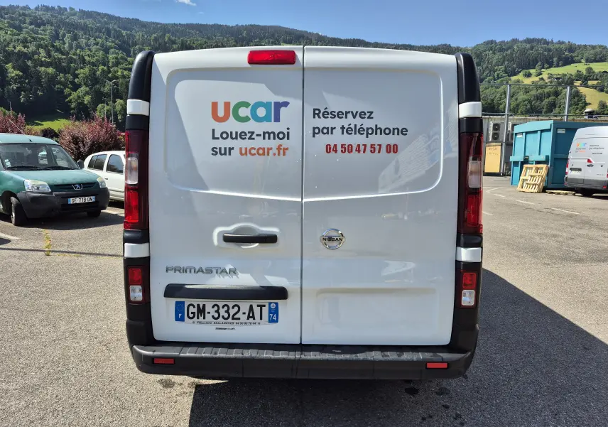 Vue arrière d’un utilitaire blanc Nissan Primastar avec marquage publicitaire ucar et numéro de téléphone de réservation.