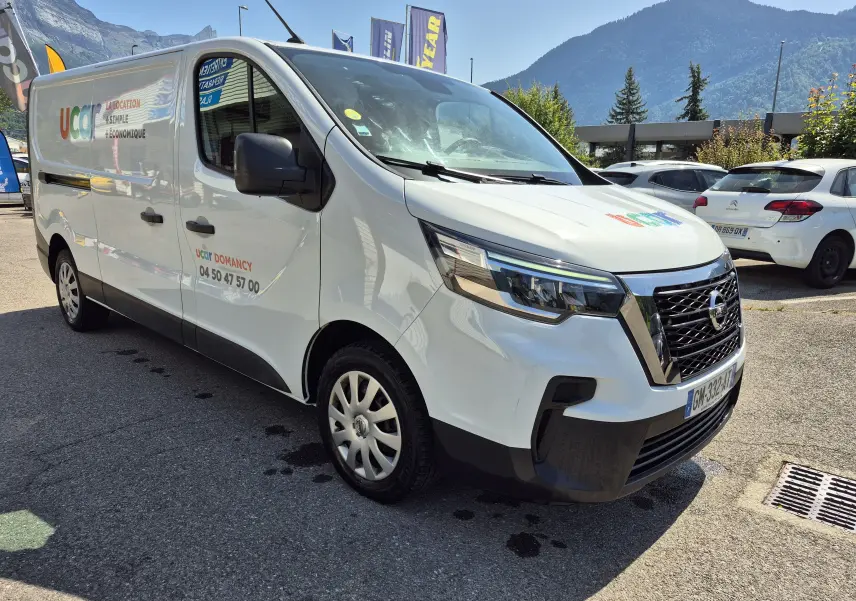 Vue 3/4 avant droit d’un utilitaire Nissan Primastar blanc avec marquage publicitaire Ucar sur porte latérale.