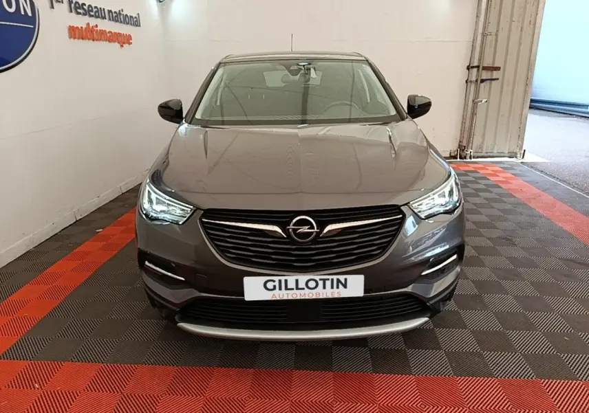 Vue frontale d'un Opel Grandland X gris foncé avec phares LED allumés, sur sol à damiers rouge et noir en intérieur.