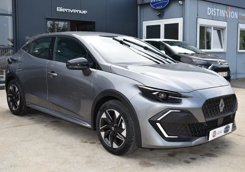 Renault Clio VI gris schiste vue 3/4 avant droit, avec calandre noire et feux LED anguleux distinctifs.