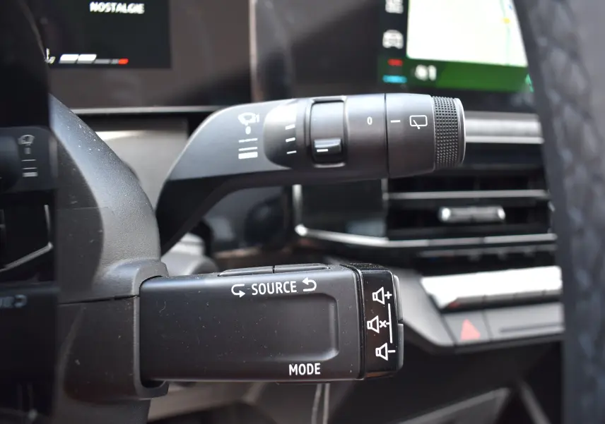 Gros plan sur la commande audio au volant de la Renault Clio VI gris schiste, avec écran tactile en arrière-plan.