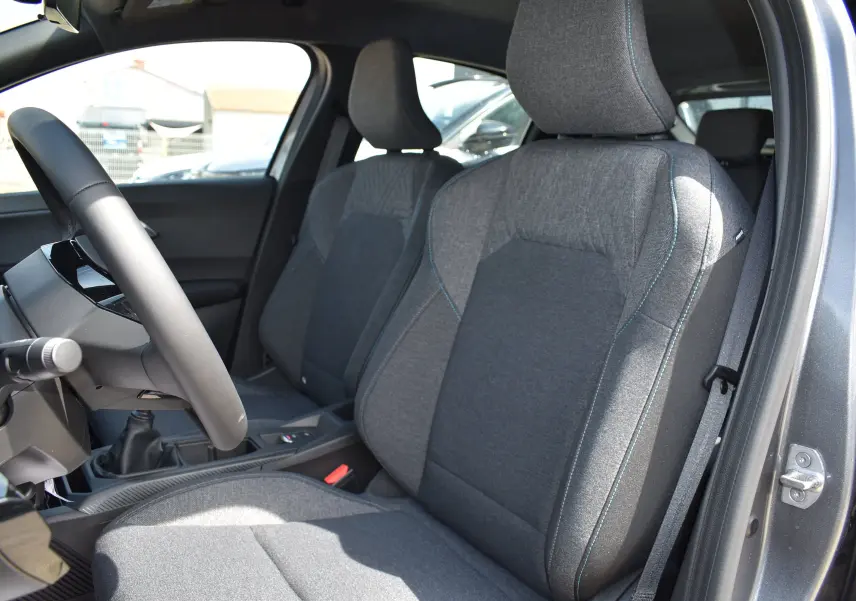 Vue intérieure côté conducteur de la Renault Clio VI gris schiste, montrant les sièges avant en tissu gris avec surpiqûres bleues.