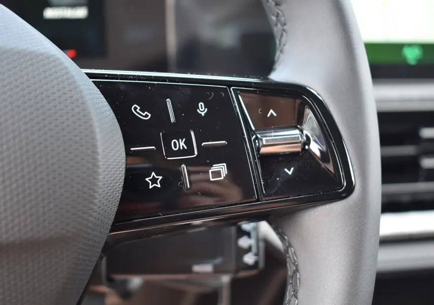 Gros plan sur les commandes multifonctions noires du volant de la Renault Clio VI gris schiste, avec touches tactiles et molette.