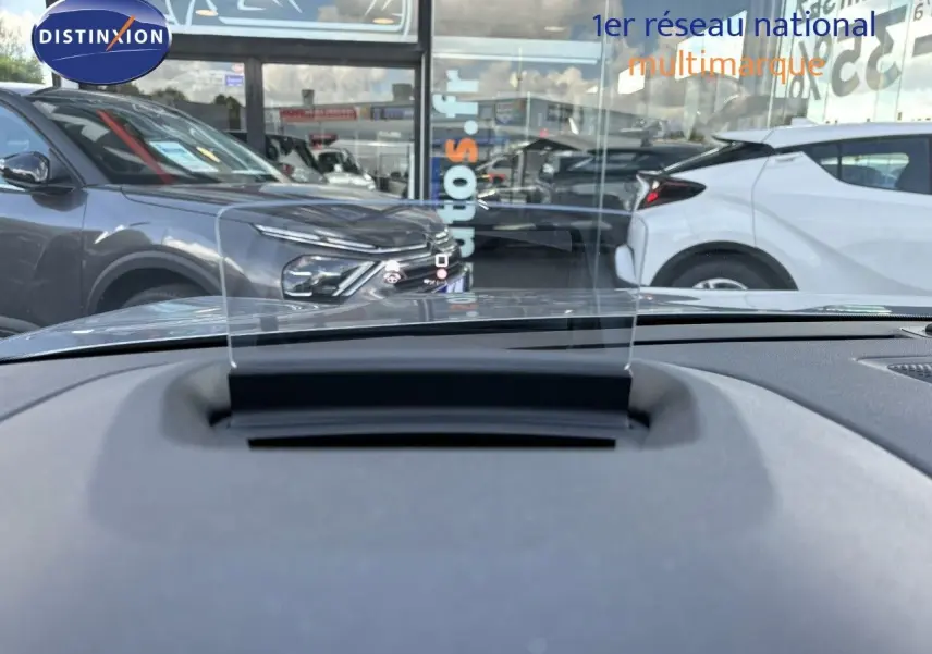 Vue depuis l'intérieur sur le tableau de bord avec affichage tête haute, devant une Citroën C4 gris Artense en 3/4 avant gauche.