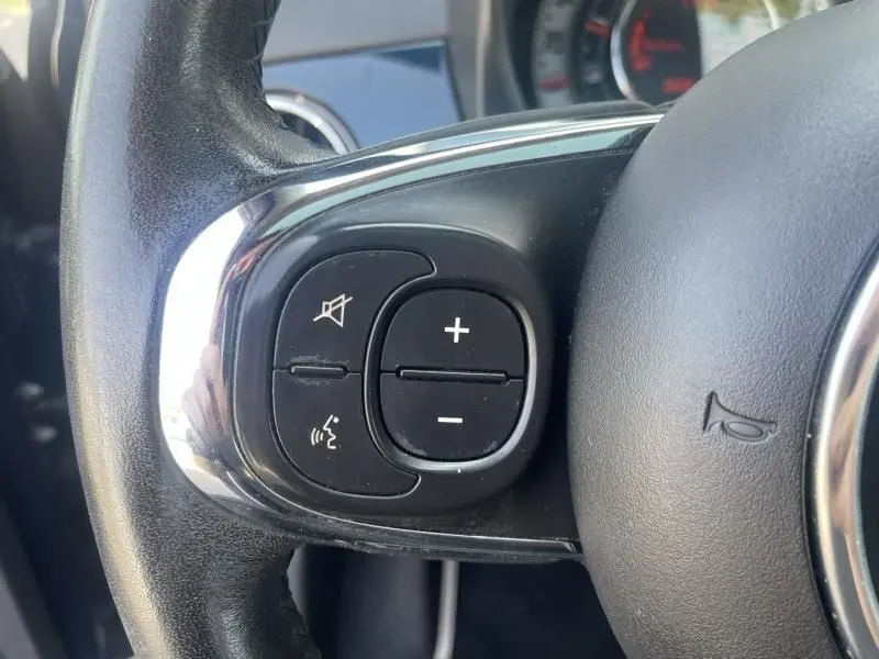 Gros plan sur les commandes audio au volant d'une Fiat 500 bleu foncé métal, modèle 2016 version Popstar diesel.