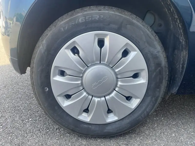 Gros plan sur la roue avant gauche d'une Fiat 500 bleu foncé métal, avec enjoliveur argenté au design distinctif.
