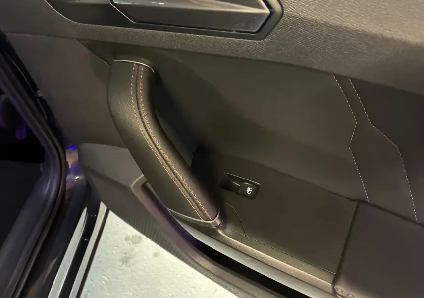 Détail de la poignée intérieure en cuir noir avec surpiqûres marron sur la porte côté gauche du CUPRA Formentor gris 2023.