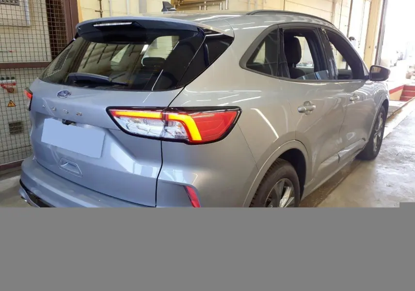 Vue 3/4 arrière droite du Ford Kuga 2.0 EcoBlue gris Solar avec feux arrière allumés en intérieur.