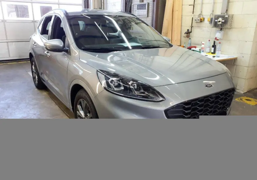 Vue 3/4 avant gauche du Ford Kuga 2024 gris Solar avec calandre noire et phares LED dans un garage.