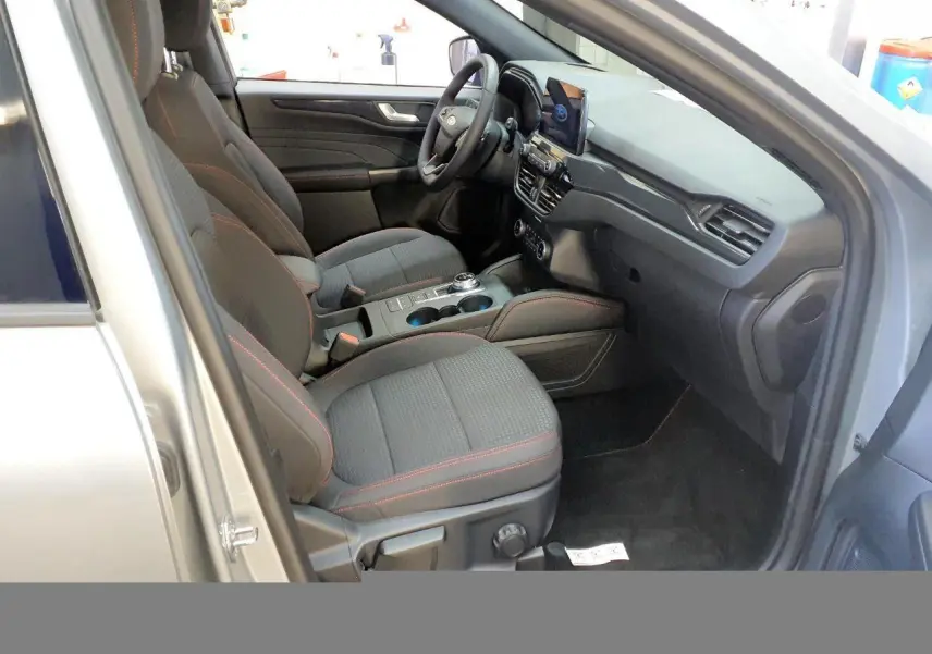 Vue intérieure côté conducteur du Ford Kuga gris Solar 2024, sièges tissu avec surpiqûres rouges et tableau de bord moderne.