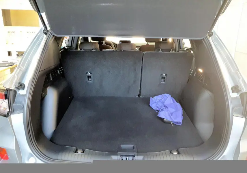 Vue arrière du coffre ouvert d'un Ford Kuga gris Solar 2024, avec banquette arrière relevée et un tissu violet posé.