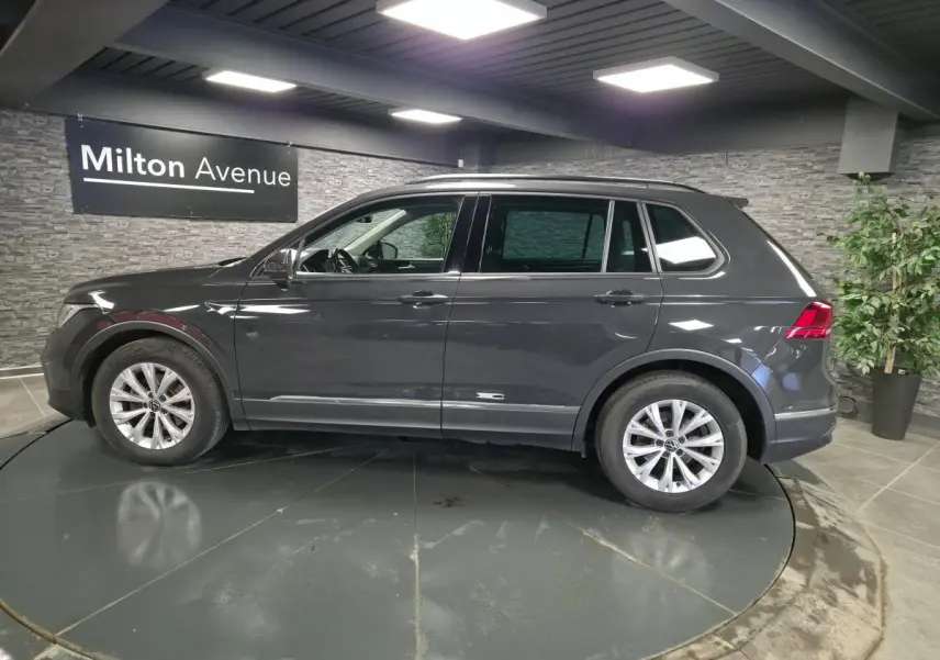 Vue de profil côté gauche d’un Volkswagen Tiguan gris métallisé 2022 dans un showroom intérieur.
