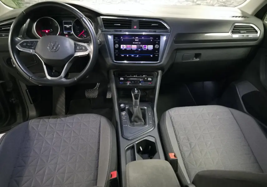 Vue intérieure frontale du tableau de bord et console centrale du Volkswagen Tiguan gris avec sellerie tissu et volant multifonctions cuir.