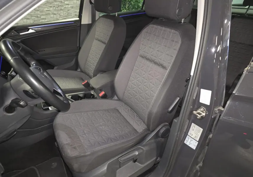 Vue intérieure côté conducteur du Volkswagen Tiguan gris 2022, sièges tissu avec motifs géométriques et éclairage d'ambiance bleu.