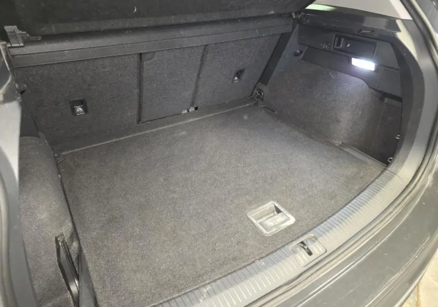Coffre ouvert du Volkswagen Tiguan gris, vue plongeante montrant le plancher et l’éclairage intérieur à droite.