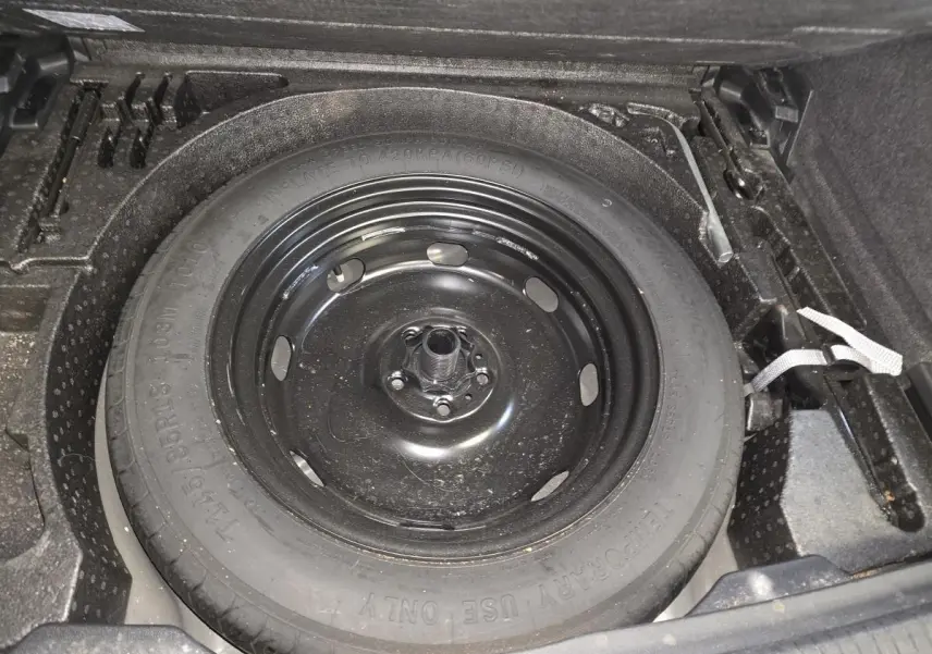 Gros plan sur la roue de secours compacte noire dans le coffre du Volkswagen Tiguan gris, version 2022.