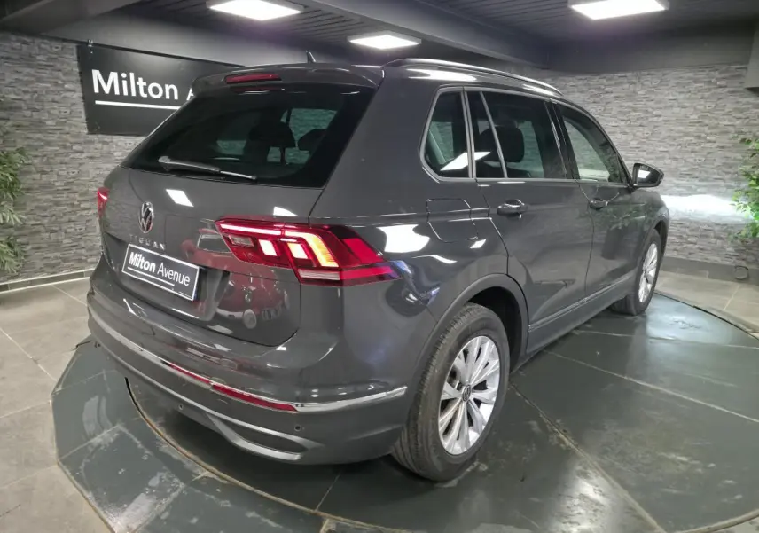 Volkswagen Tiguan gris en 3/4 arrière droit, avec feux LED et jantes alliage 17 pouces visibles en intérieur showroom.