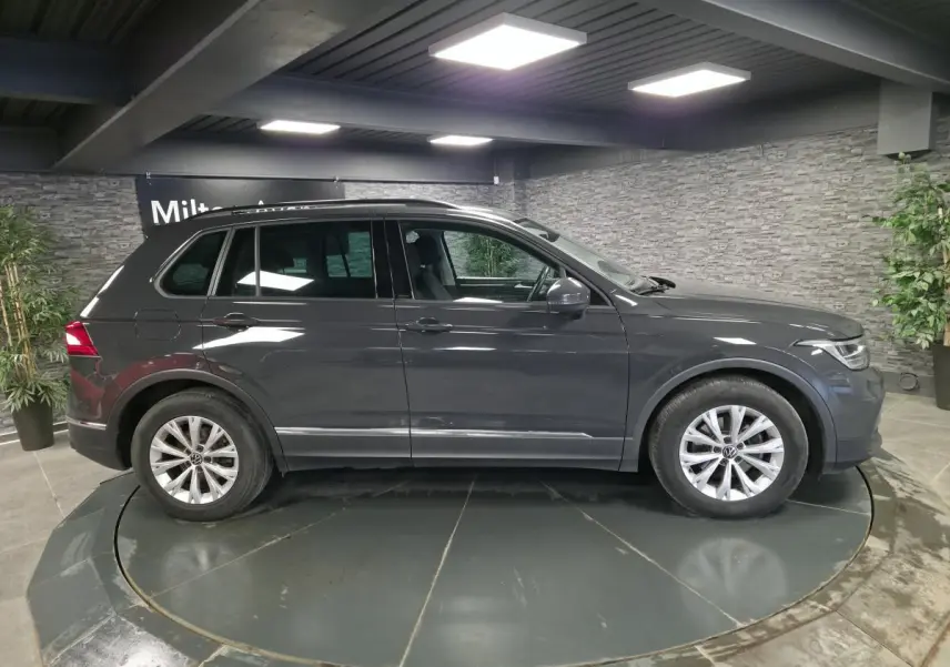 Vue latérale droite d'un Volkswagen Tiguan gris métallisé 2022 dans un showroom intérieur avec éclairage LED.