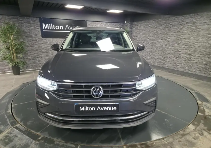 Vue avant d'un Volkswagen Tiguan gris métallisé avec feux LED allumés dans un showroom intérieur.
