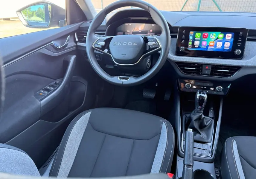 Vue intérieure avant de la Skoda Scala 2025 gris graphite, volant multifonction et écran tactile central avec connectivité smartphone.