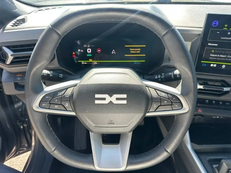 Vue rapprochée du volant multifonction noir et gris du Dacia Bigster 2025 avec tableau de bord numérique allumé.