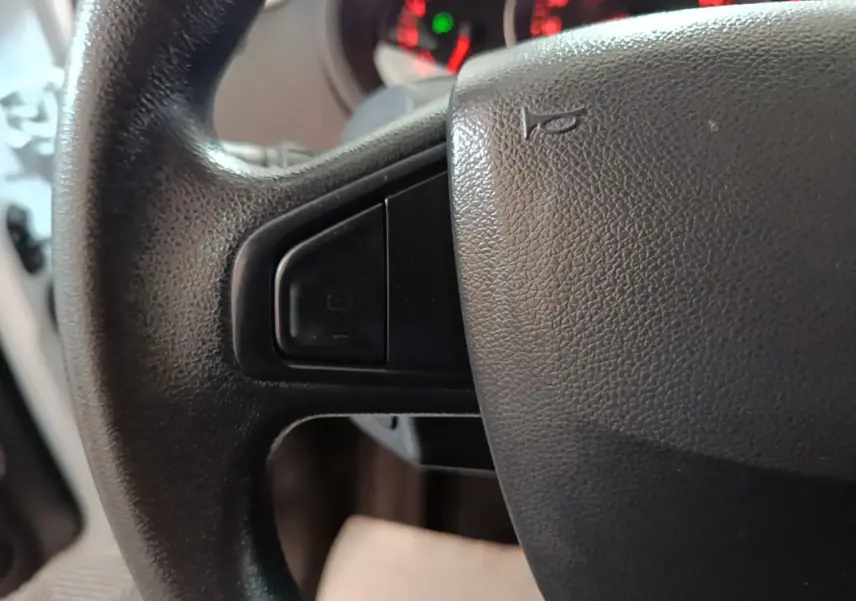Gros plan sur le volant noir du Renault Kangoo 2020 avec commandes intégrées et tableau de bord en arrière-plan flou.