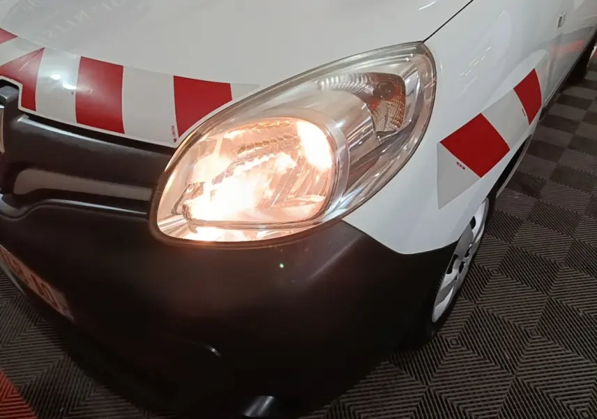 Gros plan sur l'avant droit du Renault Kangoo blanc avec phare allumé et bandes rouges réfléchissantes.