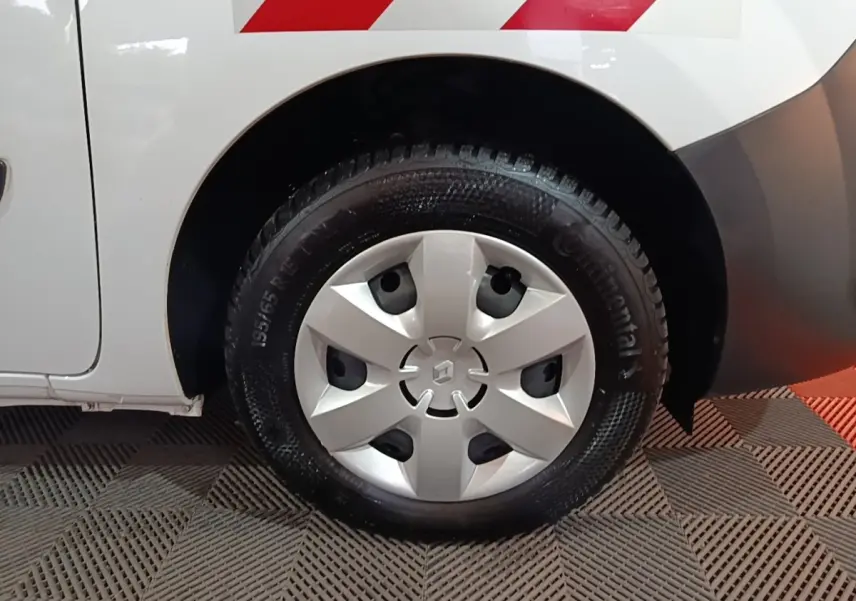 Gros plan sur la roue arrière droite blanche d’un Renault Kangoo avec enjoliveur argenté et marquage rouge sur la carrosserie.