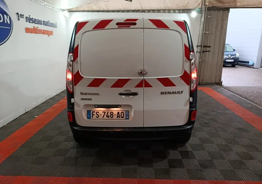 Vue arrière d’un Renault Kangoo blanc avec bandes réfléchissantes rouges et blanches, feux arrière allumés en intérieur.