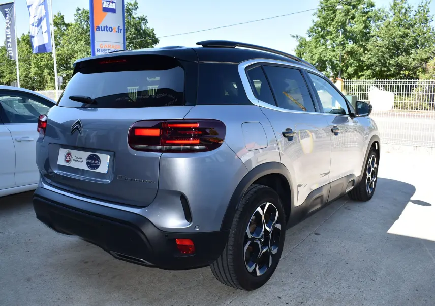 Vue 3/4 arrière droite d’un Citroën C5 Aircross 2024 gris métallisé avec toit bi-ton noir et feux arrière allumés.