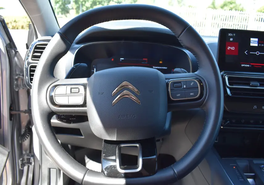 Vue rapprochée du volant noir du Citroën C5 Aircross 2024 avec tableau de bord digital et écran central tactile.