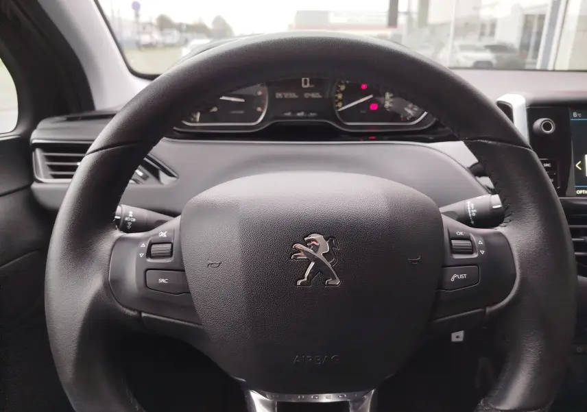Vue rapprochée du volant noir de la Peugeot 208 2019 avec commandes intégrées et tableau de bord en arrière-plan flou.