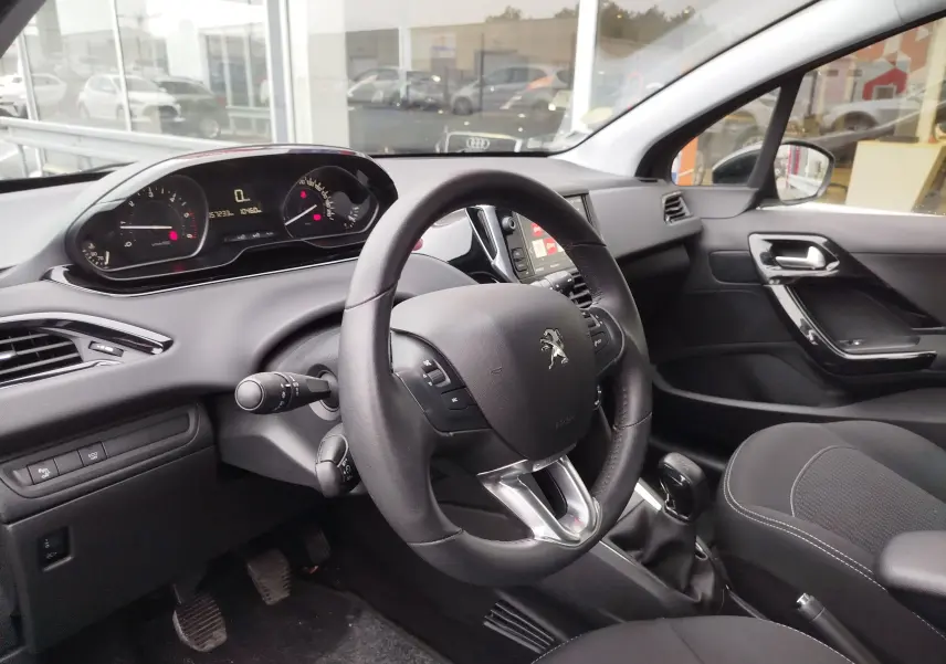 Intérieur noir de la Peugeot 208 2019, vue côté conducteur sur le volant, tableau de bord et console centrale.