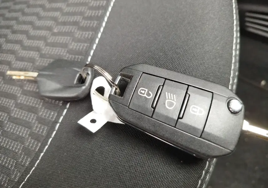 Clé de contact Peugeot 208 posée sur un siège en tissu noir, vue rapprochée du boîtier télécommande.