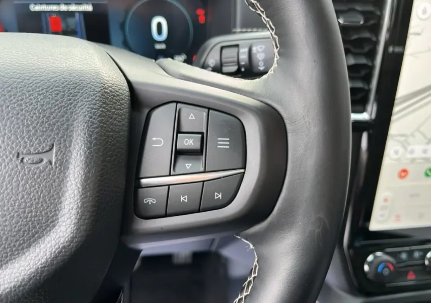 Gros plan sur le volant cuir noir du Ford Ranger 2026 avec commandes multifonctions et écran tactile visible.