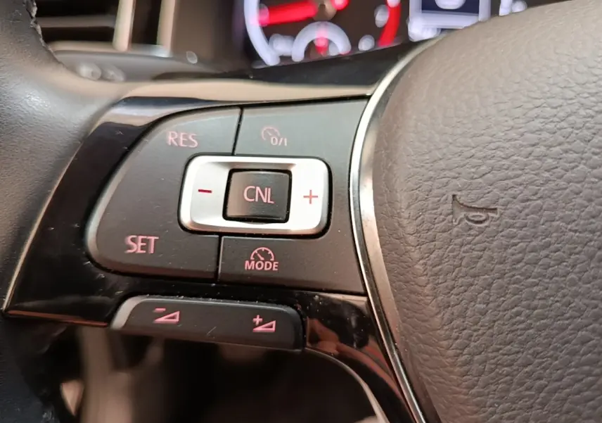 Gros plan sur les commandes du régulateur de vitesse au volant cuir d’une Volkswagen Polo noire, version Carat.