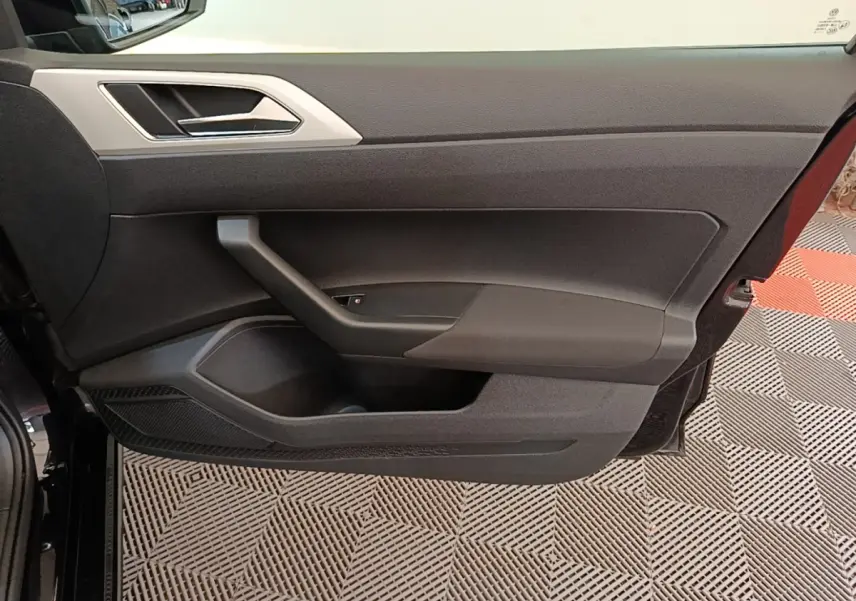 Vue intérieure de la porte avant gauche noire d'une Volkswagen Polo 2020, avec poignée argentée et rangement intégré.