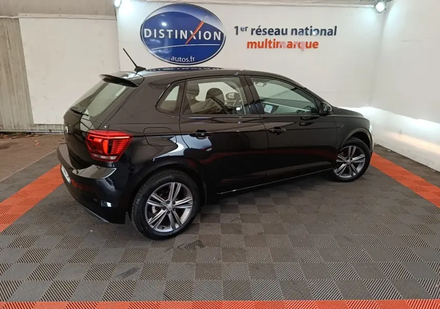 Volkswagen Polo noir vue 3/4 arrière droit en intérieur avec jantes alliage et feux arrière LED allumés.
