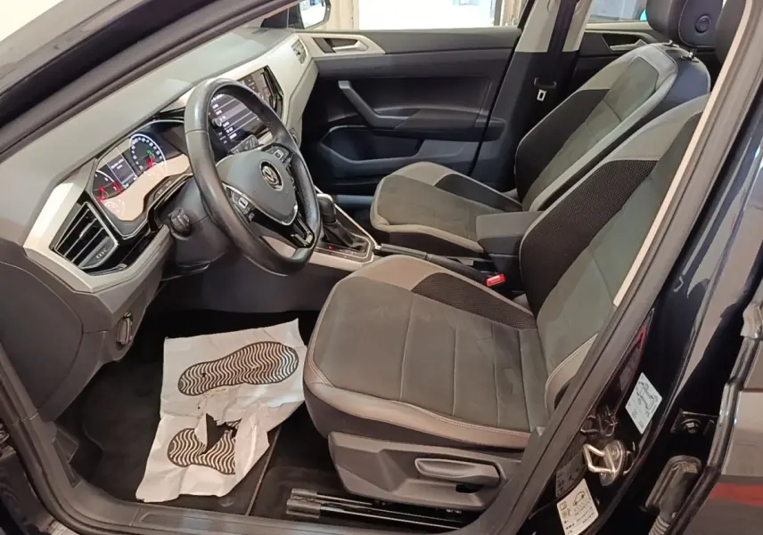 Vue intérieure côté conducteur d'une Volkswagen Polo noire 2020, montrant sièges tissu et tableau de bord moderne.