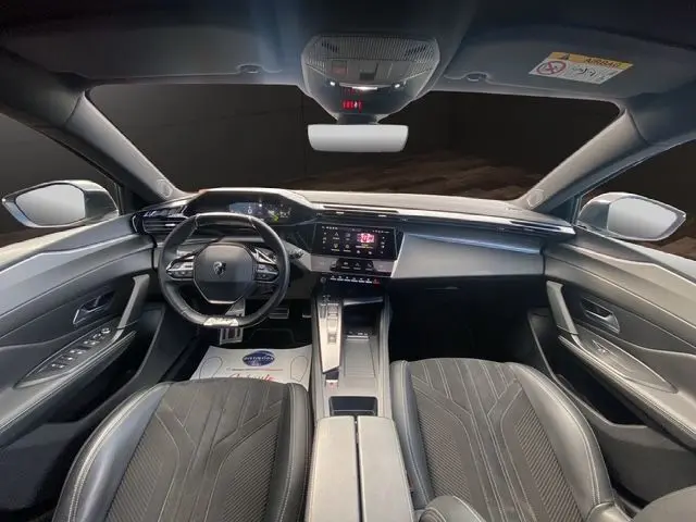 Vue intérieure avant de la Peugeot 308 SW 2022, tableau de bord moderne avec écran tactile et sièges noirs en tissu.