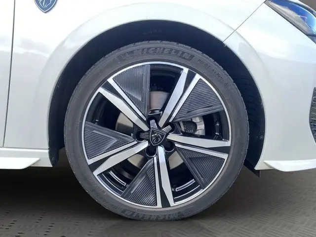 Gros plan sur la roue avant droite de la Peugeot 308 SW blanc nacré, avec jante alliage noire et argentée au design moderne.