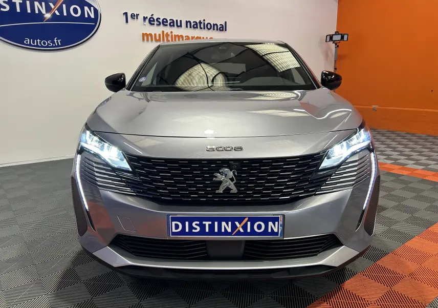 Vue avant d'un Peugeot 3008 gris 2024 avec phares LED allumés et calandre noire distinctive en showroom.