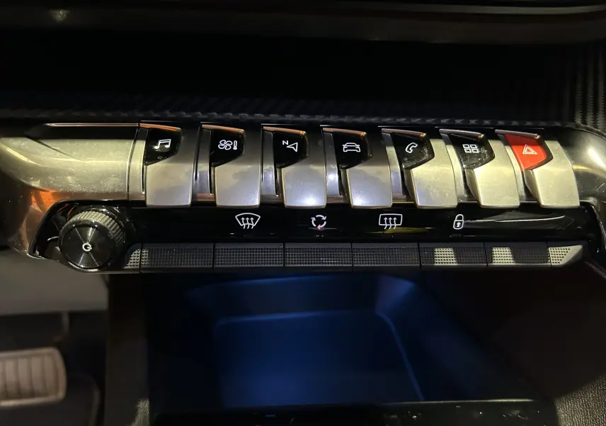 Gros plan sur la rangée de boutons de commande argentés et noirs du tableau de bord du Peugeot 3008 Hybrid 2024.