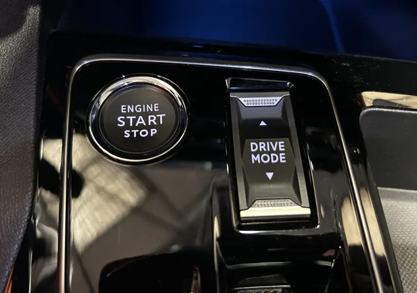 Gros plan sur le bouton start/stop et la commande drive mode du Peugeot 3008 Hybrid gris, intérieur noir brillant.