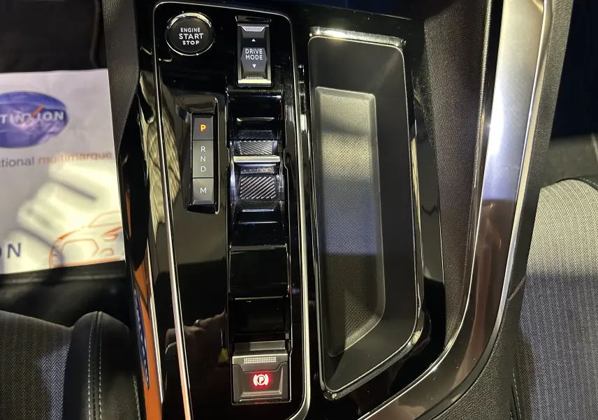 Vue rapprochée de la console centrale noire brillante du Peugeot 3008 Hybrid avec bouton start/stop et sélecteur de mode de conduite.